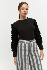 Remera negra de punto con mangas largas abullonadas con volantes.