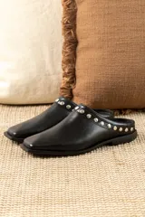 Mules de cuero negro con punta cuadrada y detalle de tachas plateadas en el borde superior.