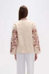 Chaqueta tipo kimono de tejido grueso color crema, con bordado floral en tonos rosados. Presenta un corte holgado y mangas anchas.