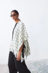 Ruana color crudo con diseño de cuadros negros y flecos en el borde inferior.