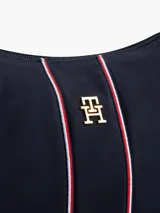 Bolso de hombro tipo hobo de nailon color azul marino, con correa de hombro ajustable de tela azul marino y detalles en cuero marrón. Presenta una franja vertical central con ribetes rojos y blancos, y un monograma TH dorado en el centro.