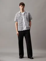 Camisa de manga corta con cuello cubano y corte boxy. Diseño con estampado de rejilla en blanco y negro y logo de Calvin Klein estampado.