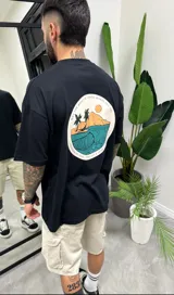 Remera negra de algodón con corte oversize y estampado en la espalda con una imagen circular de una ola, palmeras y una montaña.