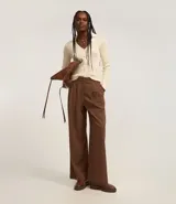 Pantalón de vestir marrón con finas rayas verticales blancas, de corte recto y tiro alto. Se ajusta a la cintura con cinturón de cuero marrón.