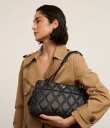 Bolso bandolera negro acolchado con patrón de rombos, asa de cadena y cierre de cremallera.