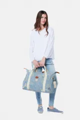Bolso tipo tote de lona color celeste con estampado de hojas en blanco, detalles en cuero marrón y correa de hombro de lona color crudo.