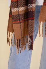 Bufanda rectangular grande con diseño escocés en tonos marrón, blanco, rojo y negro. Tiene flecos en los extremos.