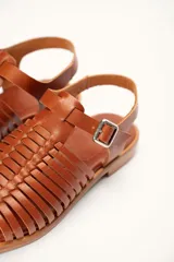 Sandalia de cuero color marrón con diseño de tiras entretejidas y hebilla lateral.