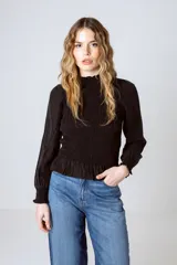 Blusa negra con cuello alto fruncido, mangas largas abullonadas y detalle de volado en el ruedo.