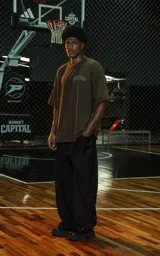 Remera de manga corta y cuello redondo, calce oversize, color marrón oscuro con efecto batik artesanal. Presenta un estampado frontal con la palabra "RAVERS" en tipografía universitaria con borde blanco.