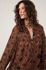 Camisa marrón con estampado geométrico de rombos negros, cuello alto, manga larga, cierre de botones, canesú con sisa descentrada y corte fruncido.
