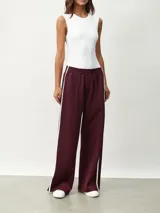 Pantalón deportivo color borgoña, de corte ancho y cintura elástica. Presenta una franja blanca vertical a lo largo de la pierna.
