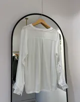 Blusa blanca de manga larga regulable, con escote en pico y botones frontales.