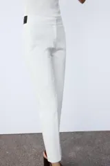 Pantalón negro tobillero de tiro medio con cintura elástica en la espalda, bolsillos delanteros y falsos bolsillos de vivo en la espalda. Bajo con aberturas laterales. Cierre frontal con cremallera, botón interior y gancho.