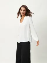 Blusa blanca de mangas largas con escote en V y textura arrugada.