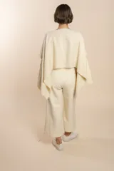 Poncho color beige con diseño a cuadros, cuello bote y terminaciones desflecadas. Tiene aberturas para los brazos en los laterales y detalles en cuero.