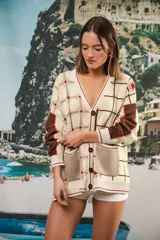 Cardigan oversized de tejido jacquard color crema con diseño de cuadrados en marrón y detalles bordados. Tiene cuello en V, cierre con botones, mangas largas y bolsillos frontales.