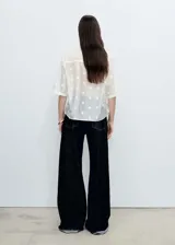 Camisa blanca semitransparente con bordado de flores blancas, de manga corta y cuello camisero.