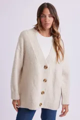 Cardigan de punto color crema, con escote en V, cierre frontal con botones marrones y corte holgado.