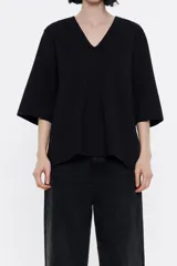 Camiseta negra de punto roma con escote en V pronunciado, manga corta y logo metálico pequeño en el frente.