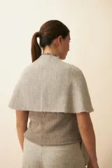 Chal asimétrico de lana color gris claro, con cortes en los hombros y doble ojal de fieltro para mantener el cruce. Terminación pespunteada y al corte.