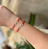 Pulsera con símbolo de infinito en metal plateado y cordón rojo ajustable.