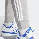 Pantalón de jogging Adidas Adicolor 3 Rayas, color gris con las tres rayas blancas a los costados. Cuenta con puños acanalados, bolsillos laterales con cierre, cintura elástica con cordón de ajuste y logo bordado.