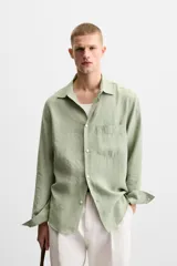 Camisa verde claro de corte relaxed fit confeccionada en tejido con mezcla de modal. Tiene cuello italiano, manga larga con puños abotonados, bolsillo de parche en el pecho y cierre frontal abotonado.