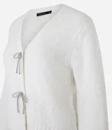 Cardigan corto color crema, de tejido tricot, con mangas largas y cierre frontal con lazos.