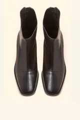 Bota corta de cuero vacuno color marrón oscuro, con diseño sin forro y taco cilíndrico de madera tallada a mano. Presenta cierre posterior y punta redondeada.