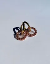 Par de aros colgantes con argollas doradas y dijes circulares de resina transparente con incrustaciones de strass de colores. El dije mide aproximadamente 1.5cm de diámetro.