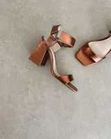 Sandalias plateadas con tira delantera, tobillera con hebilla y taco geométrico.