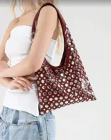 Bolso tipo tote de cuero sintético color borgoña, con apliques metálicos plateados y asa corta.