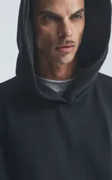 Hoodie negro de corte oversize con capucha, bolsillo tipo canguro y detalle de bolsillo con cierre en la manga izquierda.