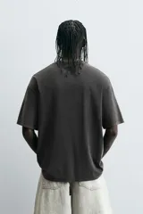 Camiseta negra de corte relaxed fit, cuello redondo y manga corta. Tiene un texto en relieve combinado a contraste en el delantero y efecto lavado.