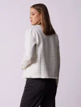 Chaqueta cruda de tejido boucle con flecos en el borde y botones negros en los puños.