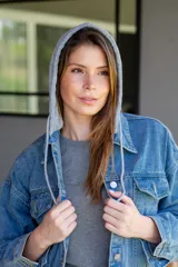 Campera de jean celeste con capucha gris de algodón desmontable, cierre con botones metálicos y bolsillos delanteros.