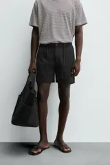 Bermuda negra regular fit confeccionada en tejido con mezcla de algodón y lino. Cintura elástica ajustable con cordón. Pliegues frontales. Bolsillos laterales y traseros de vivo. Cierre frontal con cremallera y botón.