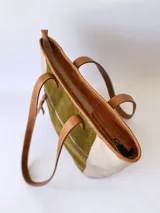 Bolso tipo tote de cuero color verde oliva con laterales de cuero texturizado color beige y manijas de cuero color marrón.