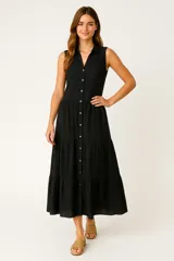 Vestido largo negro, sin mangas, con cuello camisa y abotonadura frontal completa. Presenta un diseño de volados en capas en la falda y textura de broderie.