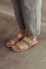 Sandalias doradas de cuero, con dos tiras anchas sobre el empeine y tobillo con hebilla lateral ajustable.