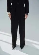 Pantalón negro de vestir, de corte recto y largo, con tiro medio, trabillas, bolsillos laterales y cierre frontal oculto con botón, gancho y cremallera. Incluye lazo ajustable en la cintura y forro interior.