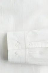 Camisa blanca de manga larga en mezcla de lyocell y algodón. Corte estándar, cuello inglés, tapeta clásica, bolsillo superior abierto, canesú con pliegue de caja en la espalda y bajo redondeado.