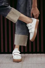 Zapatillas urbanas blancas con detalles en gris y suela color caramelo. Presentan cierre con tiras de velcro.
