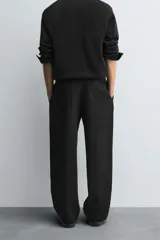 Pantalón negro de corte relajado con cintura elástica ajustable y pliegues en la parte delantera. Presenta bolsillos laterales y bolsillos traseros de parche.