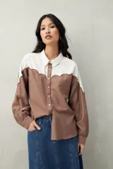 Camisa de lino color crudo y beige, con diseño bicolor y recorte ondulado en el canesú. De silueta relajada, cuenta con mangas amplias y puños camiseros. Se completa con botones de nácar.