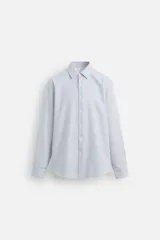 Camisa de hombre regular fit confeccionada en tejido de algodón a rayas verticales azules y blancas. Tiene cuello italiano, manga larga con puños abotonados y cierre frontal con botones.
