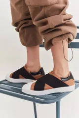 Zapatillas bajas color cuero con puntera blanca y banda elástica negra cruzada.