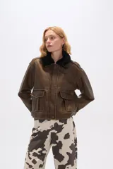 Campera marrón de eco-cuero con cuello de piel sintética negra, cierre frontal con botones a presión, bolsillos con solapa en el pecho y corte holgado.