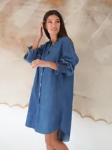 Vestido camisero corto de denim celeste, con cuello mao, mangas 3/4 con elástico en los puños y cierre frontal con botones de nácar.